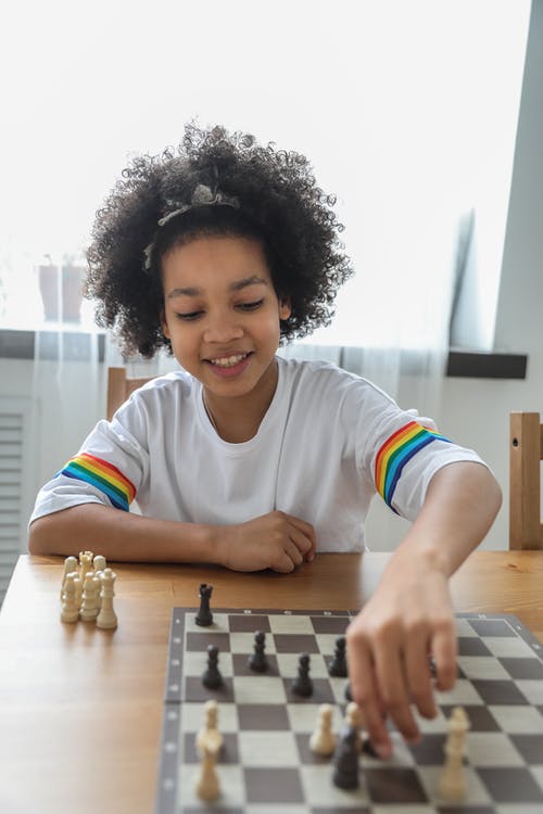 快乐的黑人女孩，在国际象棋棋盘上移动小雕像 · 免费素材图片