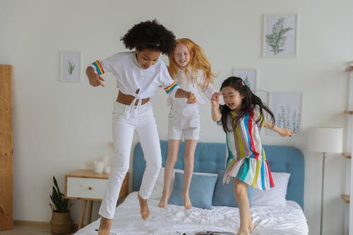 快乐的多样化女孩在跳跃在床上的休闲装 · 免费素材图片