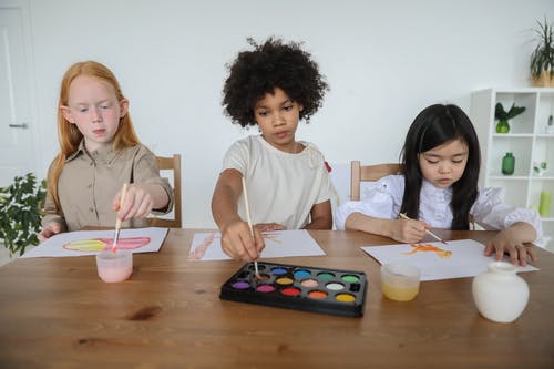 有才华的多样的小女孩坐在一起在桌上用水彩纸上绘画 · 免费素材图片