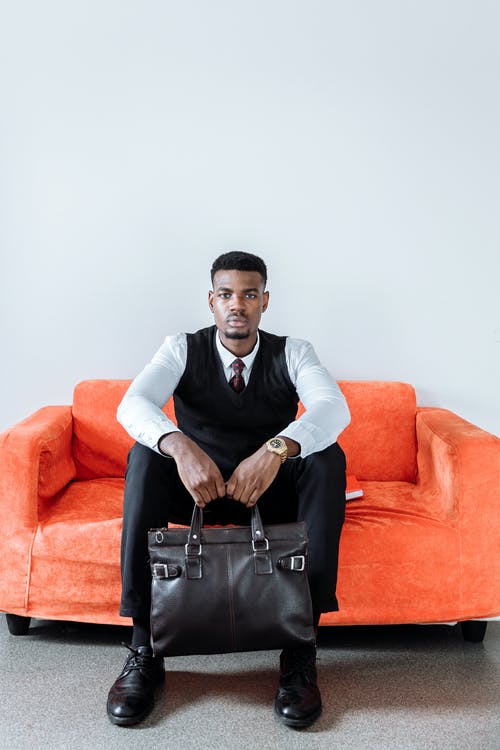 坐在橙色沙发上的黑色背心的男人 · 免费素材图片