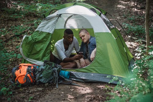 休息在有背包的绿色帐篷里的旅行的人 · 免费素材图片