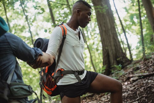 强大的民族游客帮助男性朋友沿着山坡徒步旅行 · 免费素材图片
