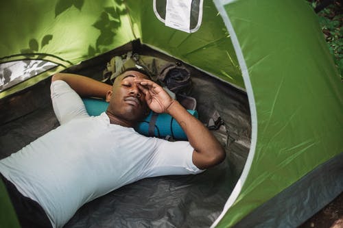 轻松的黑人男子，在自然中露营时躺在帐篷里 · 免费素材图片