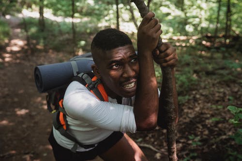 疲倦的族裔男子与背包倚在森林山上的棍子 · 免费素材图片