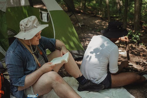 坐在绿色帐篷附近的森林里的旅游帽的朋友 · 免费素材图片
