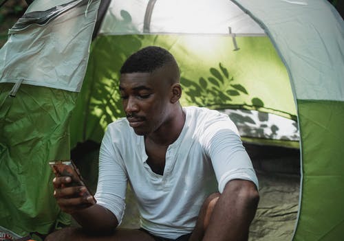 在帐篷里使用智能手机的严重黑人男子 · 免费素材图片