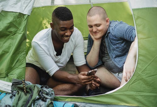 笑的人向朋友展示智能手机在帐篷里 · 免费素材图片