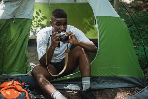 休息在有照片照相机的露营帐篷里的黑人男性旅客 · 免费素材图片