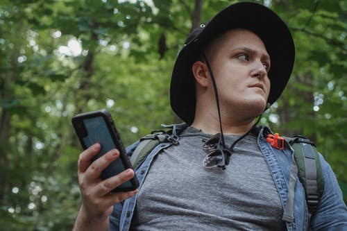 细心的徒步旅行者与智能手机在绿色的树林 · 免费素材图片