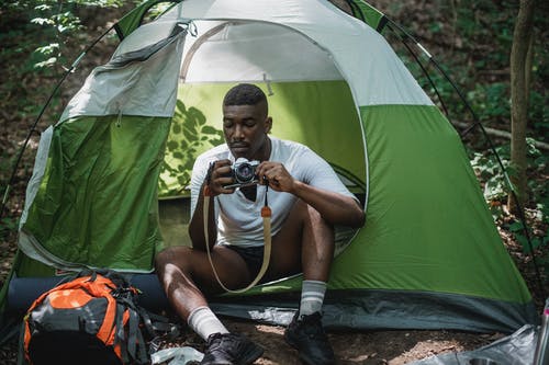 集中在帐篷里休息与照片相机的黑人男性背包客 · 免费素材图片