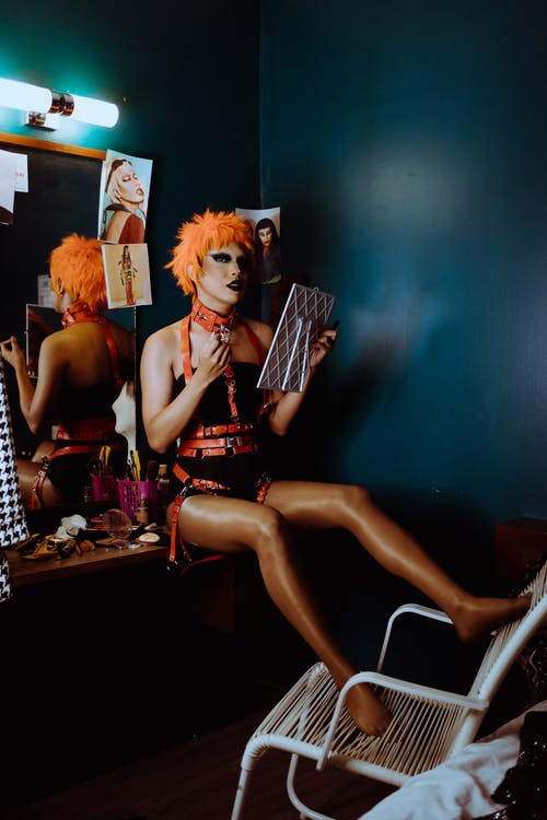 Bdsm衣服的性感年轻变性人坐在更衣室里靠近镜子 · 免费素材图片
