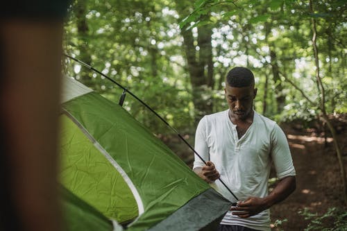体贴的黑人站在森林和建立帐篷 · 免费素材图片
