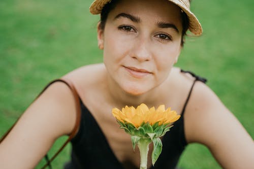 黑色背心戴棕色帽子拿着黄色花的女人 · 免费素材图片