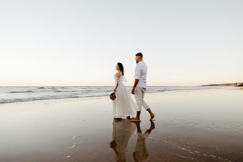 浪漫的新婚夫妇，在日落时分在沙滩上散步 · 免费素材图片