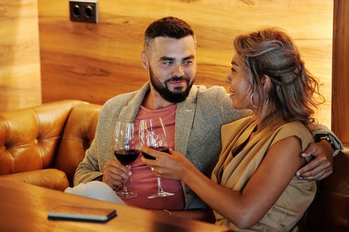 男人和女人坐在棕色的沙发，拿着酒杯 · 免费素材图片