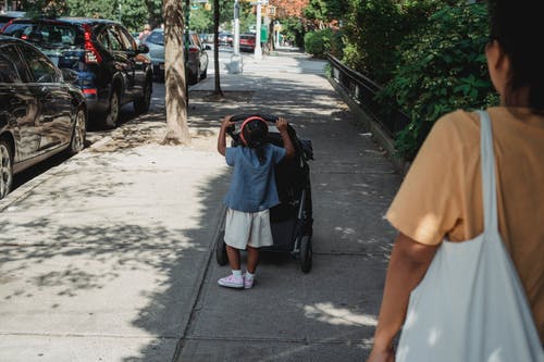 不可识别的族裔女孩推马车在人行道上 · 免费素材图片