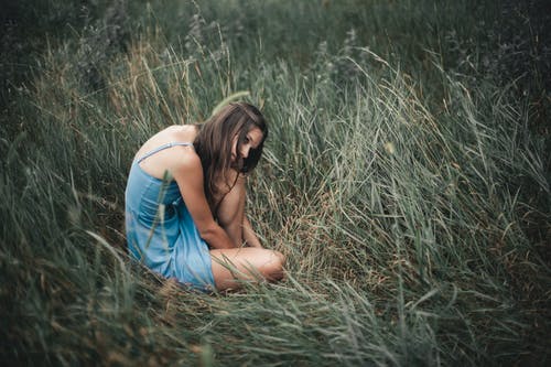 沉思的匿名女子坐在草地上 · 免费素材图片