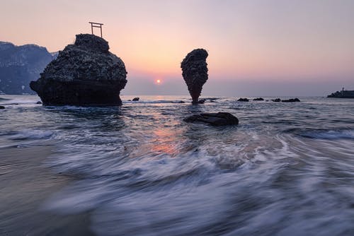 在日落时分在海岸附近的海中的悬崖 · 免费素材图片