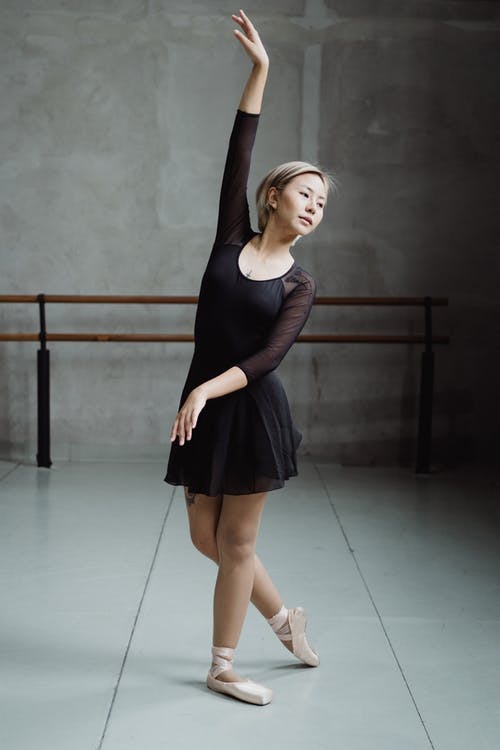 亚洲芭蕾舞演员优雅地站立，手臂在工作室里举起 · 免费素材图片