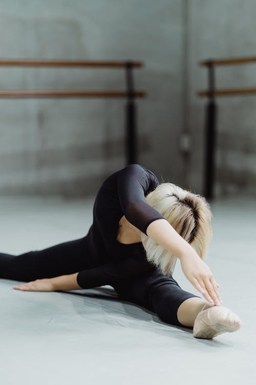 年轻的芭蕾舞演员练习分裂和弯曲到腿 · 免费素材图片