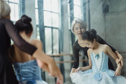 亚洲老师在做芭蕾舞动作的帮助女孩 · 免费素材图片