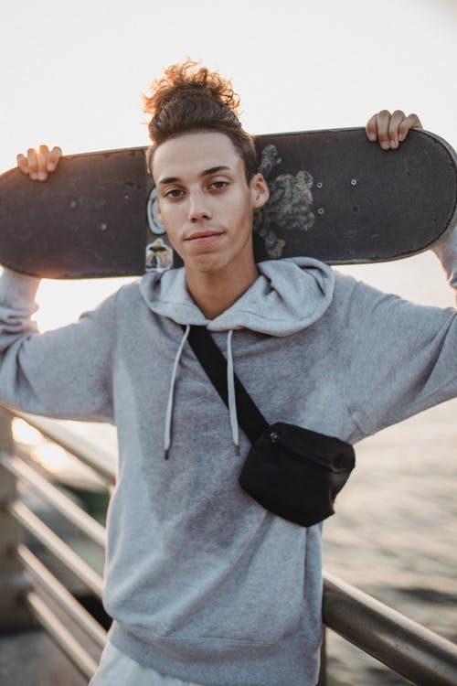 时尚伦理男性少年拿着滑板，同时站在路堤上 · 免费素材图片