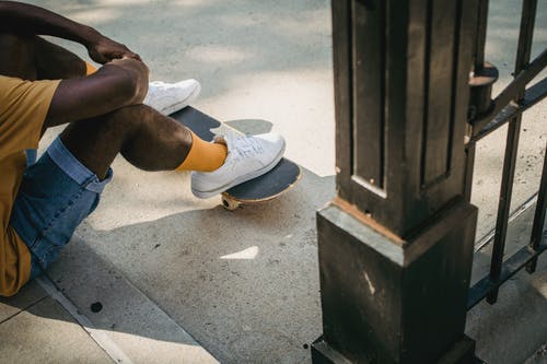 裁剪无法识别的黑人男子坐在人行道上与滑板 · 免费素材图片