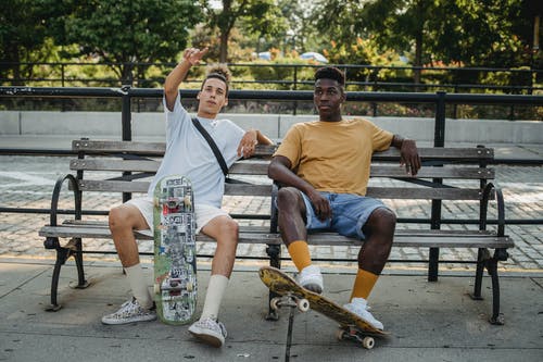 年轻人坐在长椅上与滑板在公园 · 免费素材图片