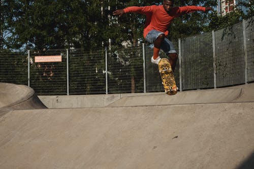 年轻的嬉戏黑人在溜冰公园在坡道上表演奥利特技 · 免费素材图片