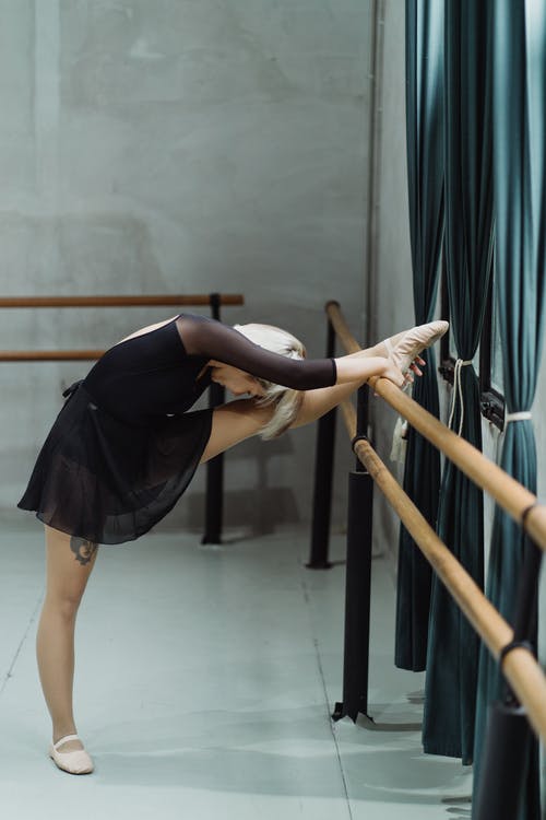 敏捷的芭蕾舞演员把腿放在巴里并伸展身体 · 免费素材图片