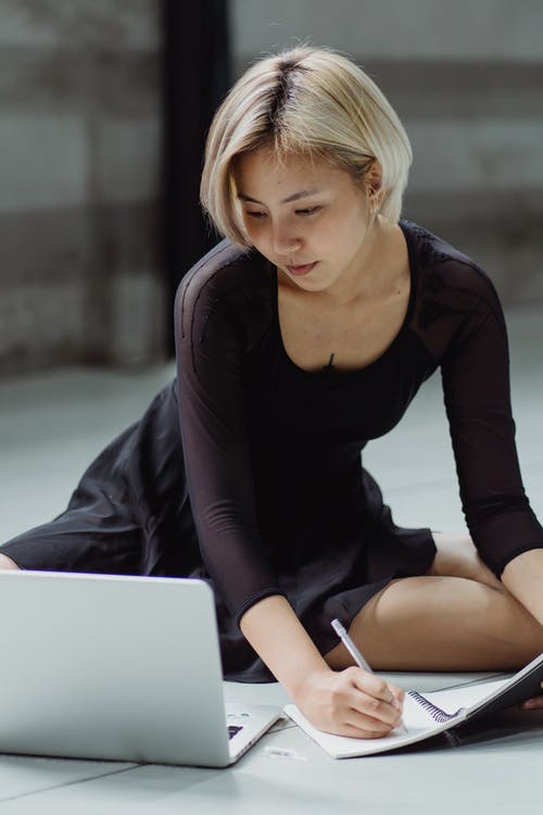 集中使用笔记本电脑和写在笔记本上的亚裔女子 · 免费素材图片