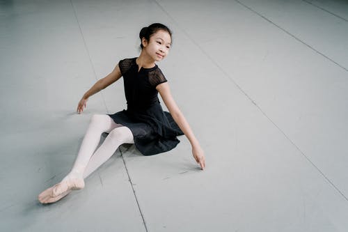 微笑的亚裔女孩芭蕾舞女演员优美地坐地板在演播室 · 免费素材图片