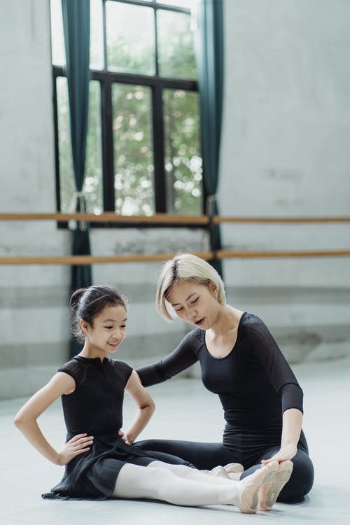 亚裔女性有芭蕾锻炼的教练员帮助的女孩在地板上 · 免费素材图片