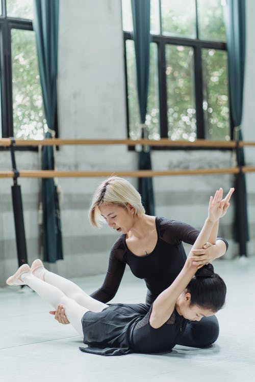 在工作室里集中与年轻的亚裔女教练做弯曲练习的小族裔芭蕾舞演员 · 免费素材图片