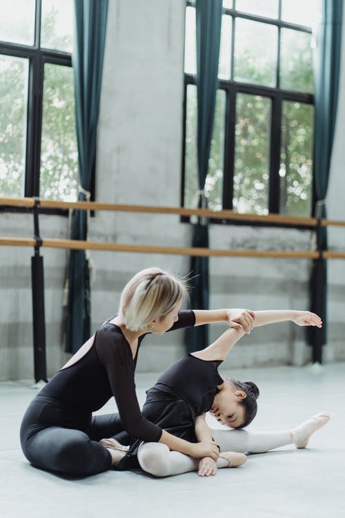 匿名教练帮助亚洲学生在芭蕾舞锻炼期间伸展 · 免费素材图片