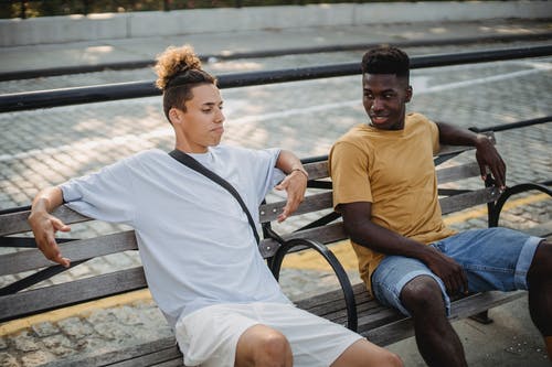 坐在长凳上与朋友沟通的积极黑人 · 免费素材图片