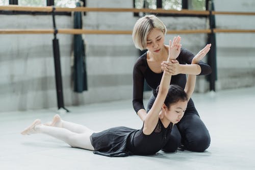 族裔芭蕾舞老师在进行芭蕾舞练习时支持女孩 · 免费素材图片