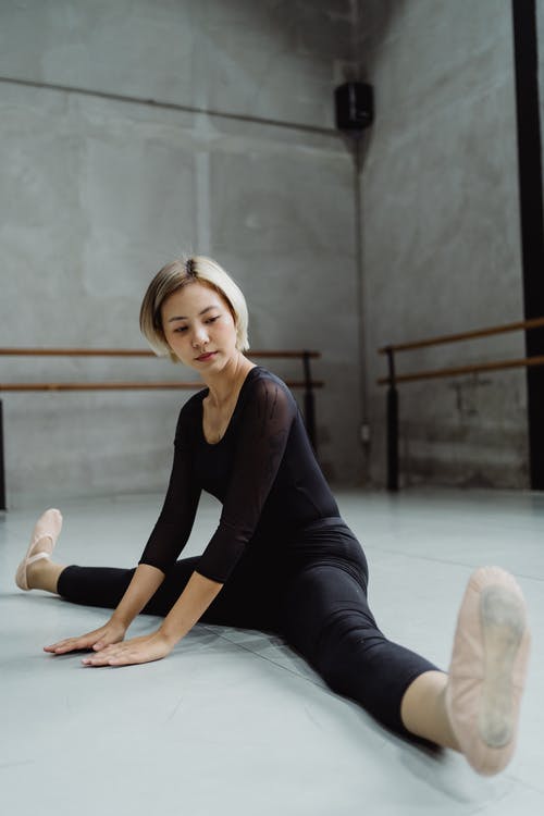 亚洲芭蕾舞女演员在地板上伸展双腿 · 免费素材图片