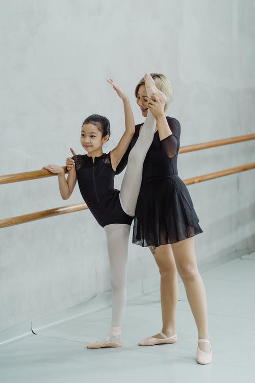 可爱的小亚洲芭蕾舞演员在与女老师的训练期间伸展臀部近巴里 · 免费素材图片