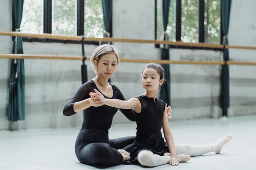 在锻炼期间的亚裔女性芭蕾舞女演员帮助的女孩在地板上 · 免费素材图片
