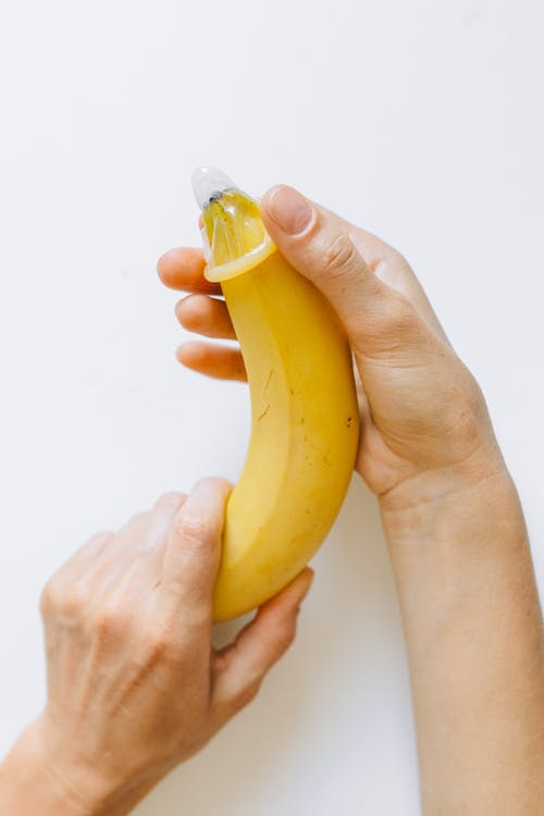 在香蕉上包裹避孕套的人 · 免费素材图片