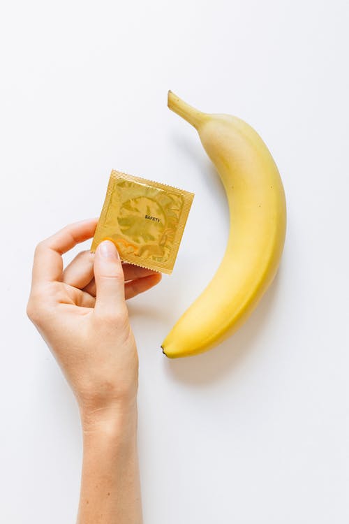 香蕉旁边持有避孕套的人 · 免费素材图片