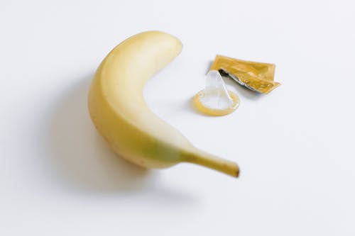 香蕉旁边的解开的避孕套 · 免费素材图片