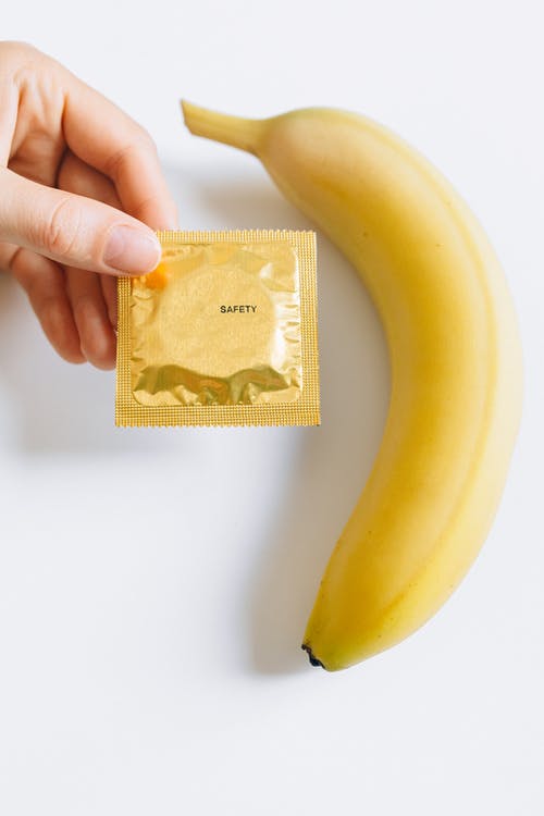 香蕉旁边持有避孕套的人 · 免费素材图片