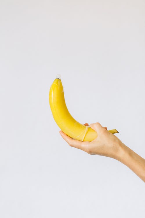 持有香蕉包裹在避孕套中的人 · 免费素材图片
