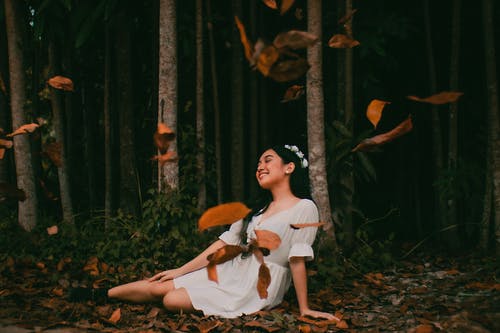 叶子落下时坐在地上的白色连衣裙的女人 · 免费素材图片