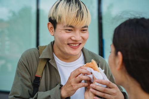 作物女人手用热狗喂开朗的亚洲男朋友 · 免费素材图片
