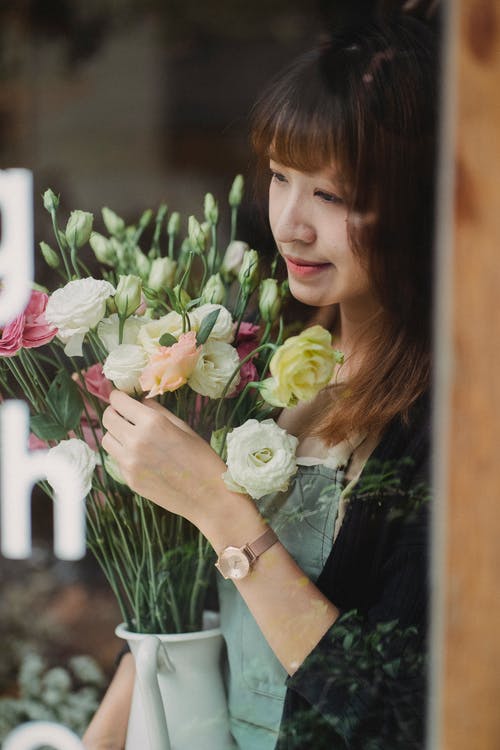 作物宁静的亚洲女人站在花瓶里盛开的鲜花 · 免费素材图片