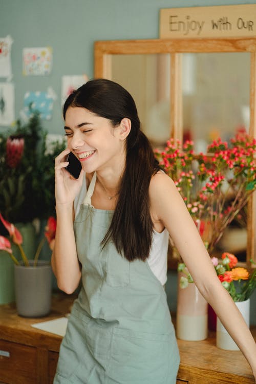微笑的女人在花店里的电话上说 · 免费素材图片