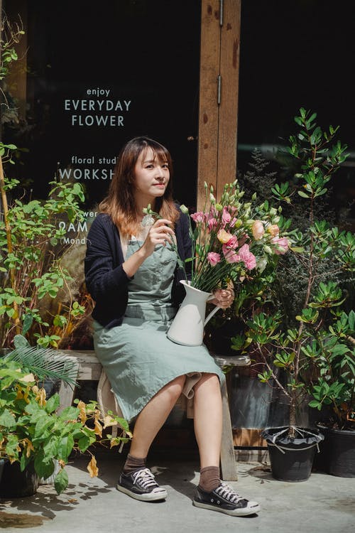 美满的亚洲女性花店，坐在长椅上与花束 · 免费素材图片